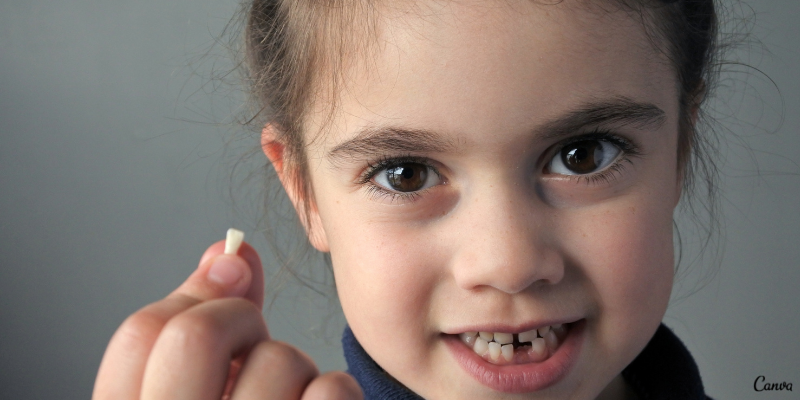 imagem de rosto de menina sorrindo sem um dente incisivo, que ela mostra segurando entre os dedos