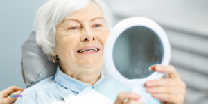 mulher idosa olhando admirando no espelho seu implante dentário